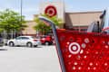 Red shopping cart in a parking lot with cars and a store entrance in the background.
