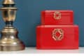 Brass lamp and red decorative boxes on white dresser with gold knobs against a blue wall.