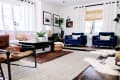 Living room with blue velvet armchairs, a gray sofa, patterned rugs, plants, and framed art on white walls.