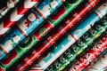 Colorful rolls of Christmas wrapping paper featuring snowmen, candy canes, and festive patterns.