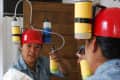 Person cleaning a mirror wearing a red helmet with attached cleaning bottles, using a cloth and spray.