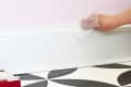 A person uses a dryer sheet to remove dust from baseboards