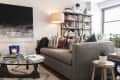Cozy living room with a gray sofa, patterned pillows, bookshelves, abstract art, and a glass coffee table with candles.