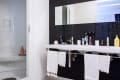Modern bathroom with black tile backsplash, double sink, toiletries, and white towels hanging below.