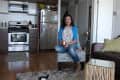 Woman sitting in a living room with a Boston Terrier on a rug, near a kitchen with stainless steel appliances.