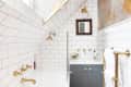 Bathroom with white subway tiles, gold fixtures, a small vanity, and floral wallpaper under a sloped ceiling.
