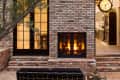 Brick patio with a central fireplace, flanked by glass doors leading to a dining room and kitchen with a large clock.