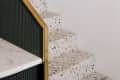 Terrazzo stairs with multicolored speckles and a brass-accented black railing next to a marble countertop.