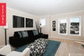 Living room with black sofa, patterned ottoman, blue rug, abstract wall art, and large windows.
