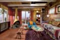 Retro living room with wood paneling, vintage TV, hanging fireplace, colorful sofa, and patterned curtains.