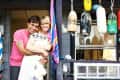 Couple embracing on porch with colorful buoys, potted succulents, and a striped towel hanging on railing.
