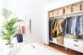 Open closet with organized clothes, wicker baskets, and a potted plant in a bright bedroom.