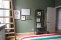 Loft bedroom with green walls, ladder, framed art, and a black shelf holding decor items and a folded blanket.