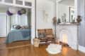 Bedroom with blue bedding, paper lanterns, wooden bench, and ornate white fireplace with decorative items.
