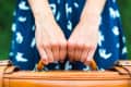 Hands gripping a leather suitcase handle, wearing a blue dress with white bird patterns.