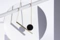 Gold chain necklace with a black circle and bar pendant, casting shadows on geometric white shapes.