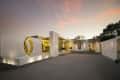 Modern house exterior at sunset with a large gold ring sculpture, marble walls, and landscaped entrance.