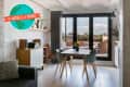 Modern living room with a dining table, gray chairs, large windows, and a balcony view.