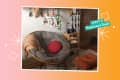 Cozy corner with a gray papasan chair, red cushion, orange throw, small bookshelf, and wall art.