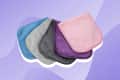 Five microfiber cloths in blue, gray, black, purple, and pink on a purple background.