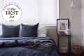 Cozy bedroom with dark blue bedding, two pillows, a framed portrait on a side table, and a woven basket.