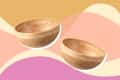 Two wooden bowls on a colorful abstract background with pink, yellow, and beige waves.