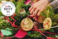 Hands decorating a Christmas tree with gold ornaments and red ribbons.