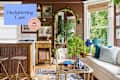 Cozy living space with a beige sofa, blue and white decor, plants, and a wooden kitchen bar.