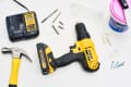 Yellow and black DeWalt drill with charger, Stanley hammer, drill bits, screws, and spackling paste on a white surface.