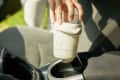 Hand placing a glass wrapped in a white sock into a car cup holder.