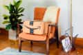 Orange chair with Amazon package, plant, knit blanket, and magazine rack in a cozy room setting.