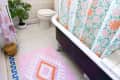 A bathroom with a floral shower curtain and patterned rug.