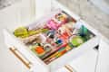 Open kitchen drawer with assorted items including scissors, pens, tape, string, and a Band-Aid box.