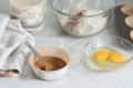 Baking ingredients on a counter with eggs, flour, cinnamon, and cupcake liners.