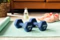 Dumbbells on a yoga mat in the living room with sneakers and water bottle nearby