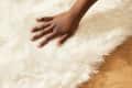 close up shot of someone's hands in the process of cleaning their shag rug by smoothing fibers