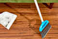 overhead shot of a white and blue broom sweeping up dirt on the hardwood floor.