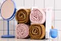 Rolled pink and brown towels stacked in a white holder next to a blue mirror and a blue candle.
