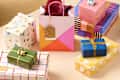 Colorful wrapped gifts in various patterns, including a pink bag with a tag, arranged on a light surface.