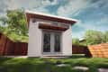 Modern backyard shed with glass double doors, wooden awning, and surrounding wooden fence.