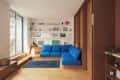 Modern living room with blue sectional sofa, wooden floors, built-in shelves, and large windows.
