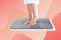 Feet standing on a gray memory foam bath mat against a pink abstract background.