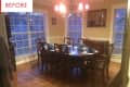 Traditional dining room with wooden table, eight chairs, blue tableware, chandelier, and large windows.