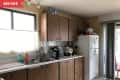 Cluttered kitchen with brown cabinets, white fridge, and various items on the counter, including a coffee maker and cleaning supplies.