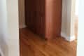 Tall wooden cabinet with six doors in a narrow hallway, hardwood floor.