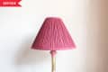 Brass table lamp with a pink pleated shade on a wooden surface.