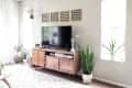Living room with a wooden TV stand, potted plants, and geometric wall art above the television.