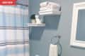 Small bathroom with blue walls, striped shower curtain, white shelves, towels, and decorative plant.