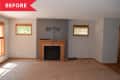 Empty living room with beige carpet, wooden fireplace, gray accent wall, and two small windows with blinds.