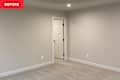 Empty room with light gray walls, carpeted floor, and a closed white door on the right.